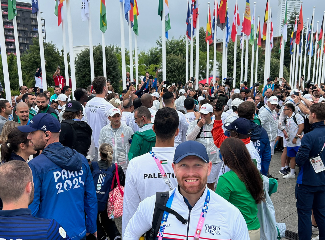 A man smiles posing in front of the flags of the Olympics. 