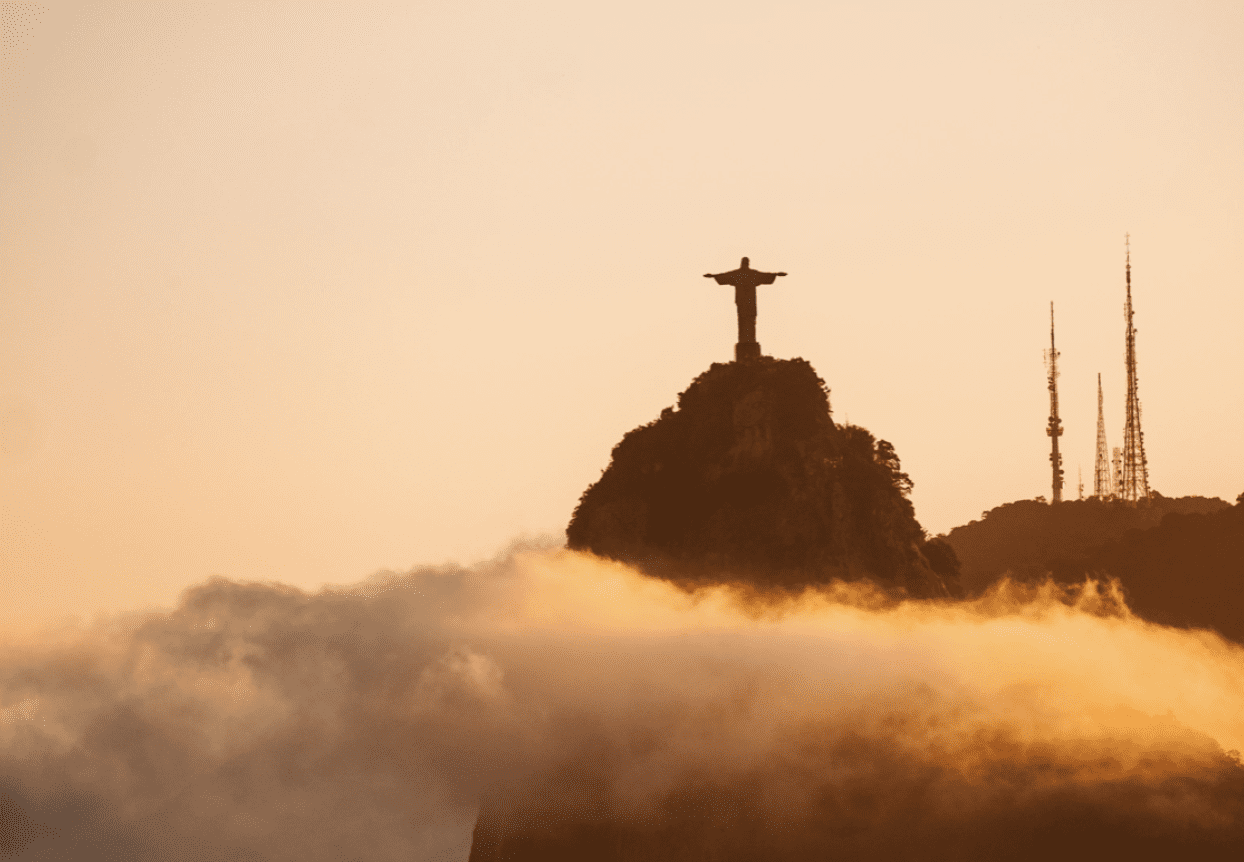 An image taken at sunset of Christ the Redeemer in Brazil, with clouds surrounding the statue. 