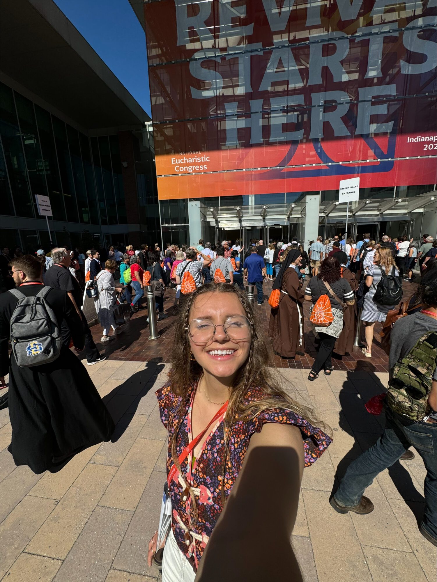 The image shows a young woman posing for a selfie at the National Eucharistic Congress. 