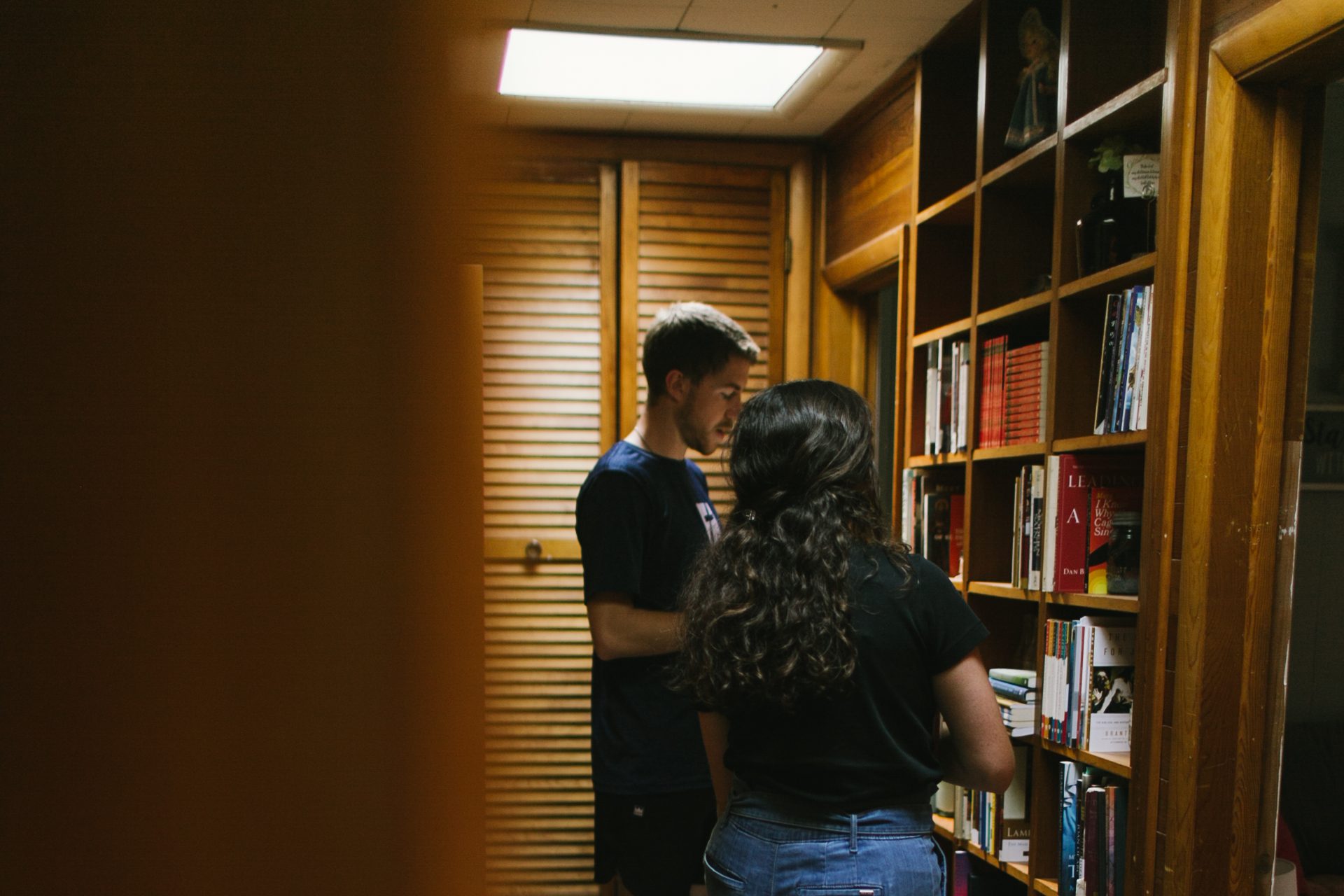 A man and woman look at Catholic books together in a bookshelf.