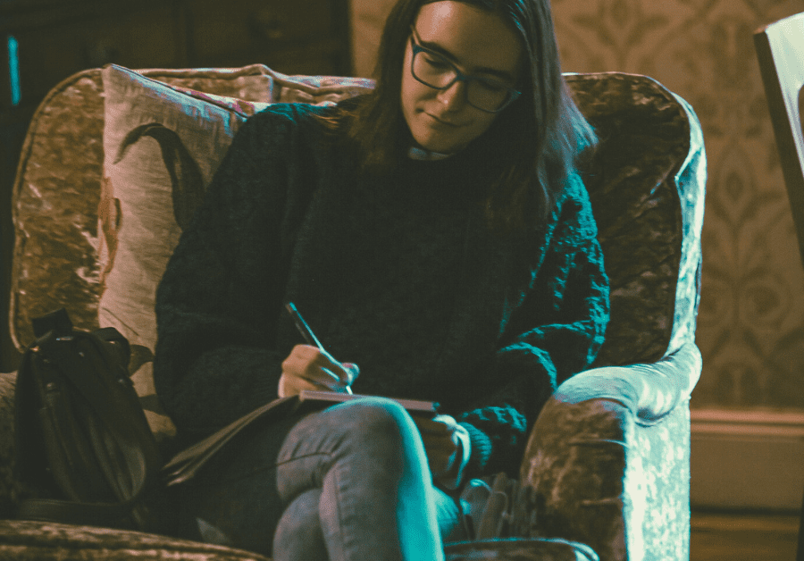 A girl writes in her prayer journal sitting in a chair. 