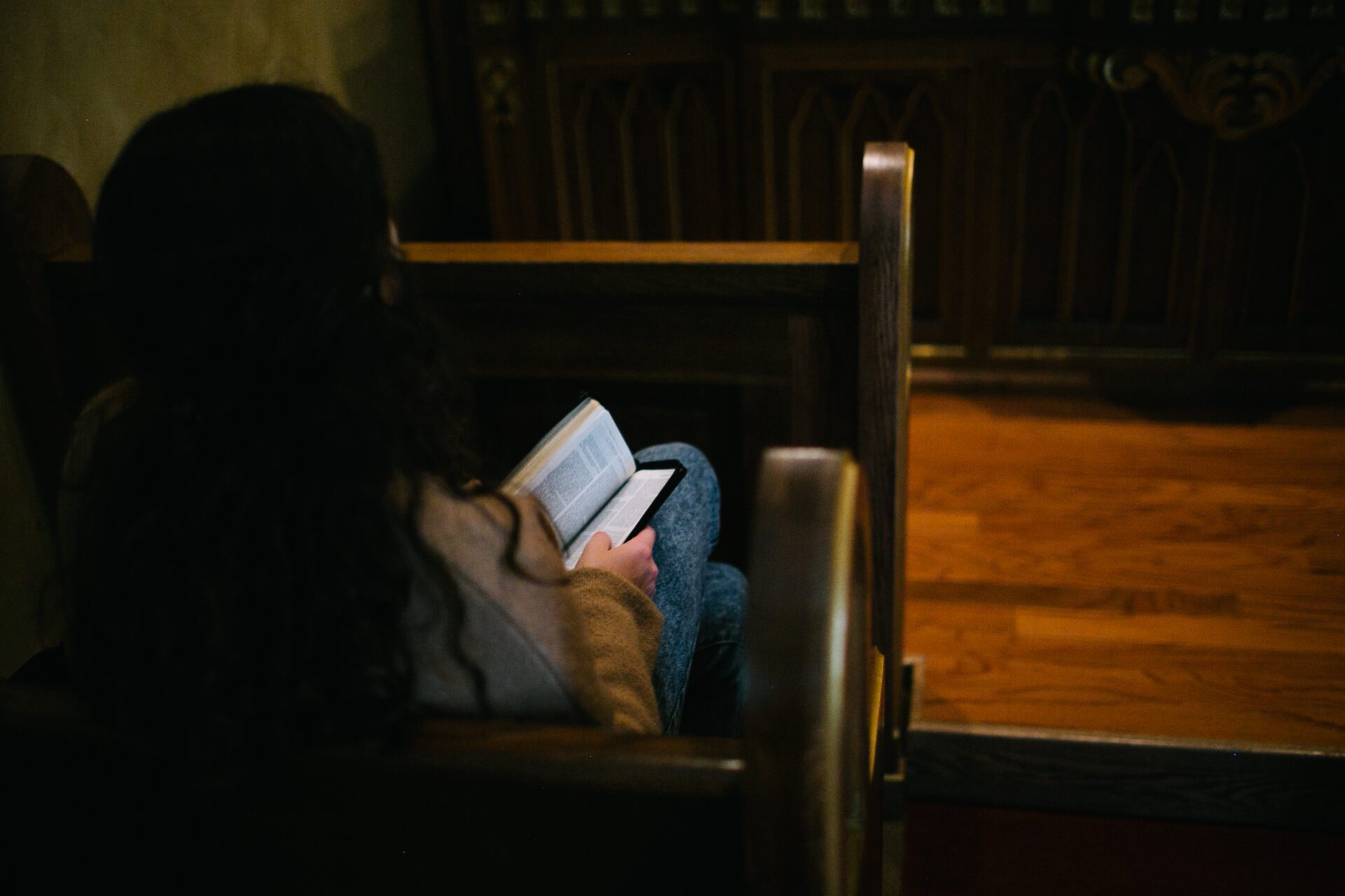 A girl prays in a pew in a sacred space. She reads a Bible. 