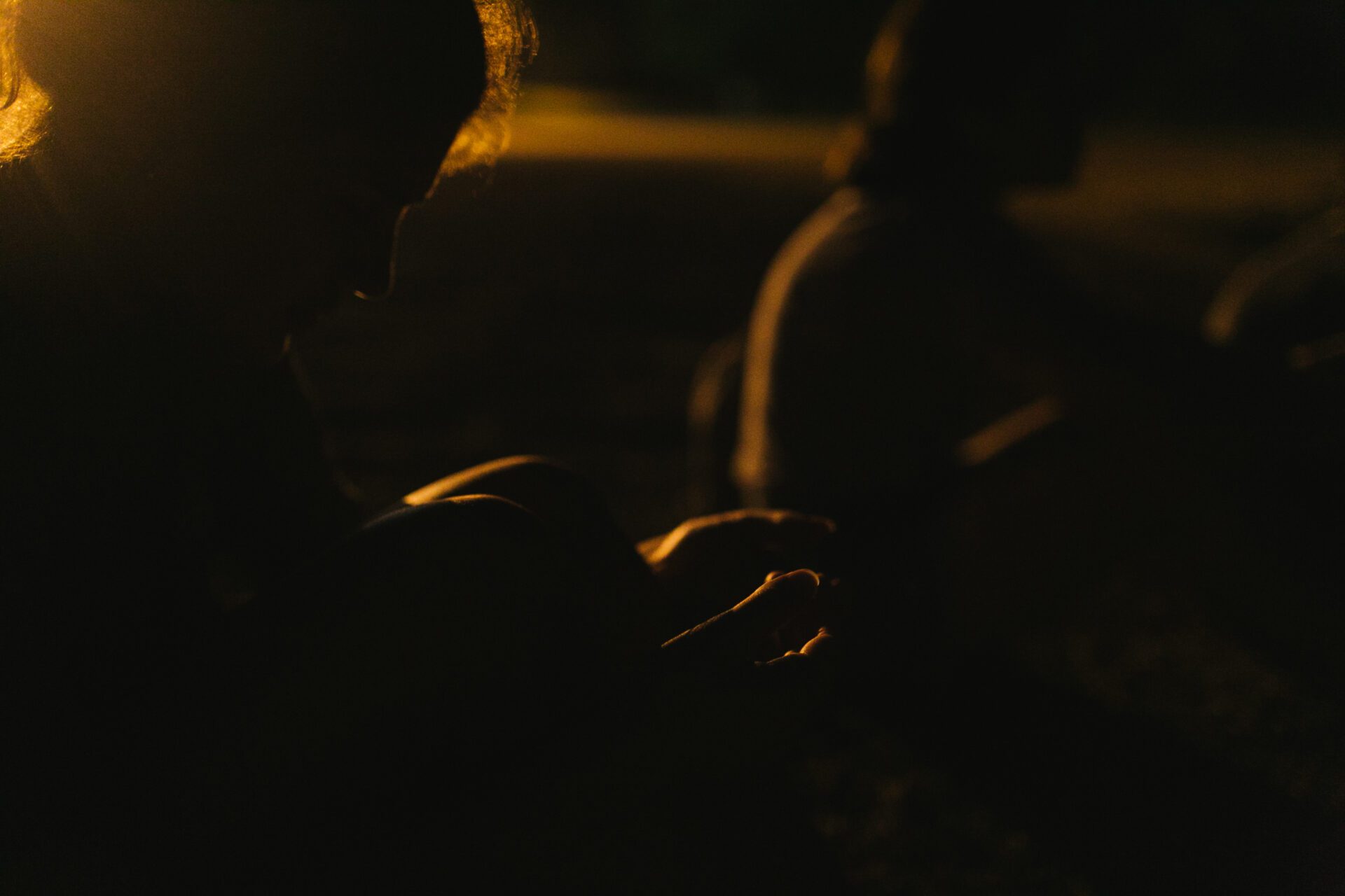 A couple prays in a dimly lit space, with orange evening light glowing through the window. 