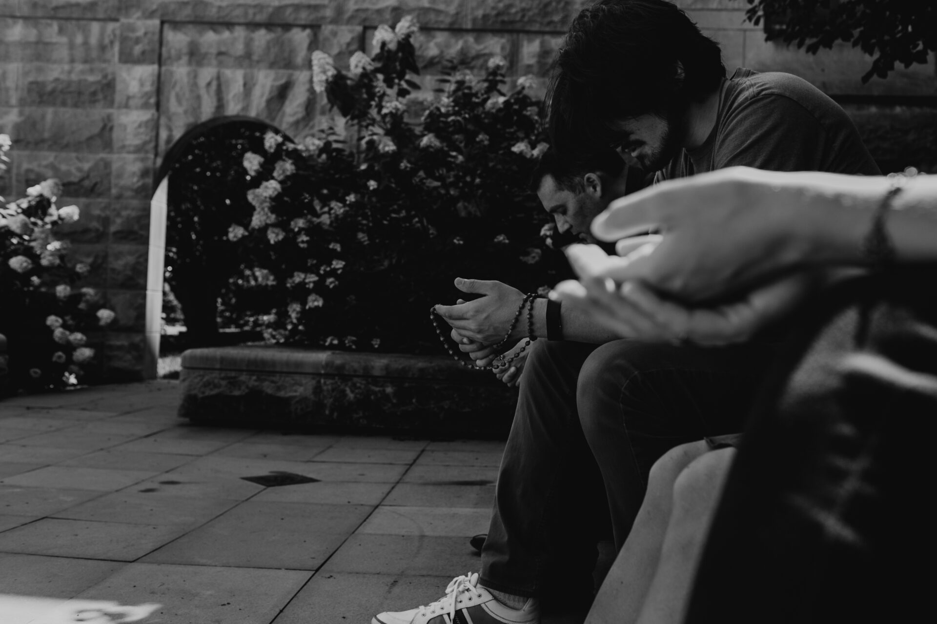 Friends pray in a courtyard space holding rosaries. 